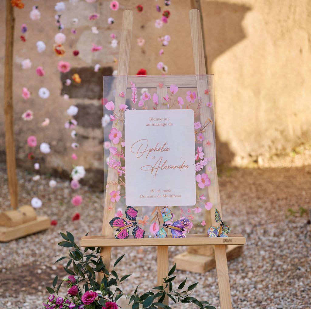 Panneau de bienvenue de mariage en plexiglass, décoré de fleurs roses et oranges.