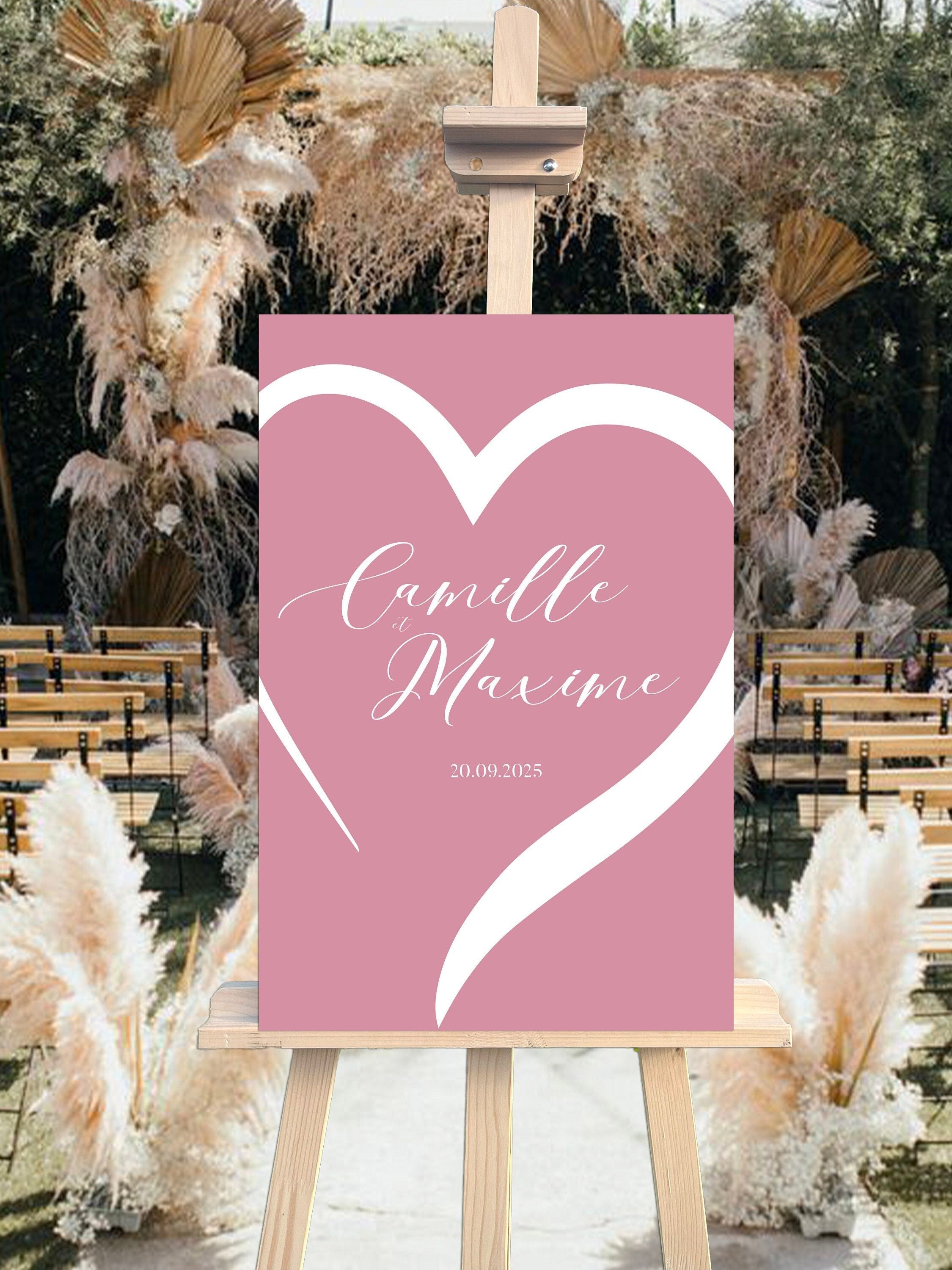 Panneau de bienvenue mariage en forex rose poudré, personnalisé avec prénoms, lieu et date, décoré d’un cœur pour une ambiance romantique et moderne.