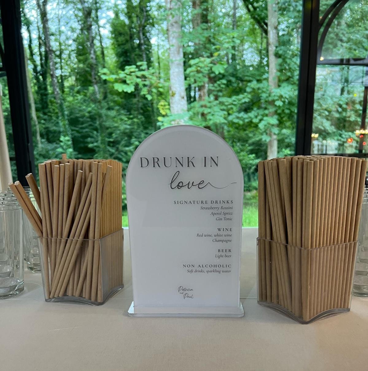 Menu de mariage en forme d’arche en plexiglass blanc, personnalisable avec prénoms et date, design élégant pour bar ou coin cocktails Modèle "Drunk in love"