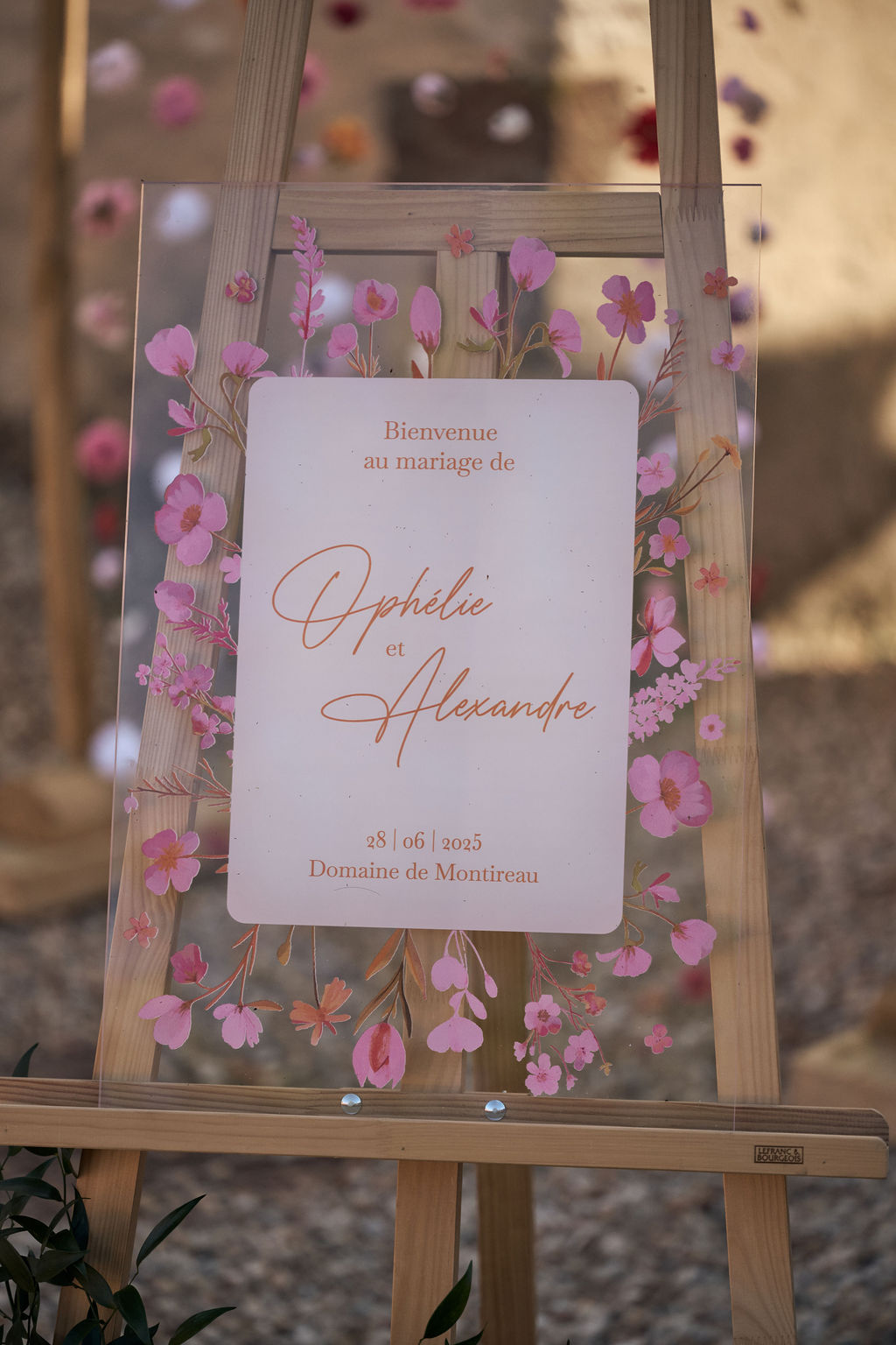 Panneau de bienvenue en plexiglass transparent avec fleurs oranges et roses, idéal pour guider les invités lors de la réception de mariage