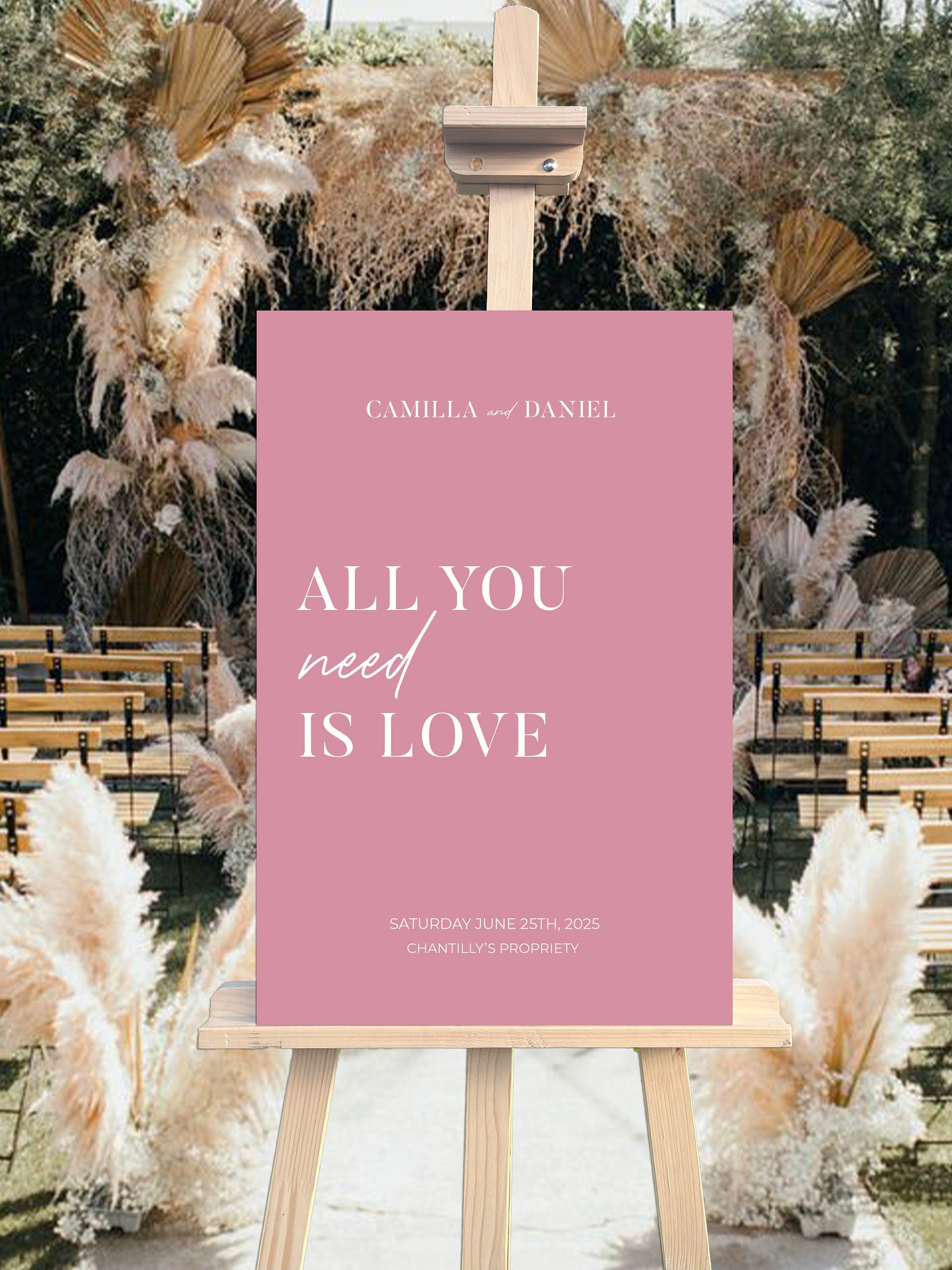 Panneau de bienvenue mariage en forex rose poudré, personnalisé avec prénoms, lieu et date, décoré de la citation "All you need is love" pour une ambiance romantique et moderne.