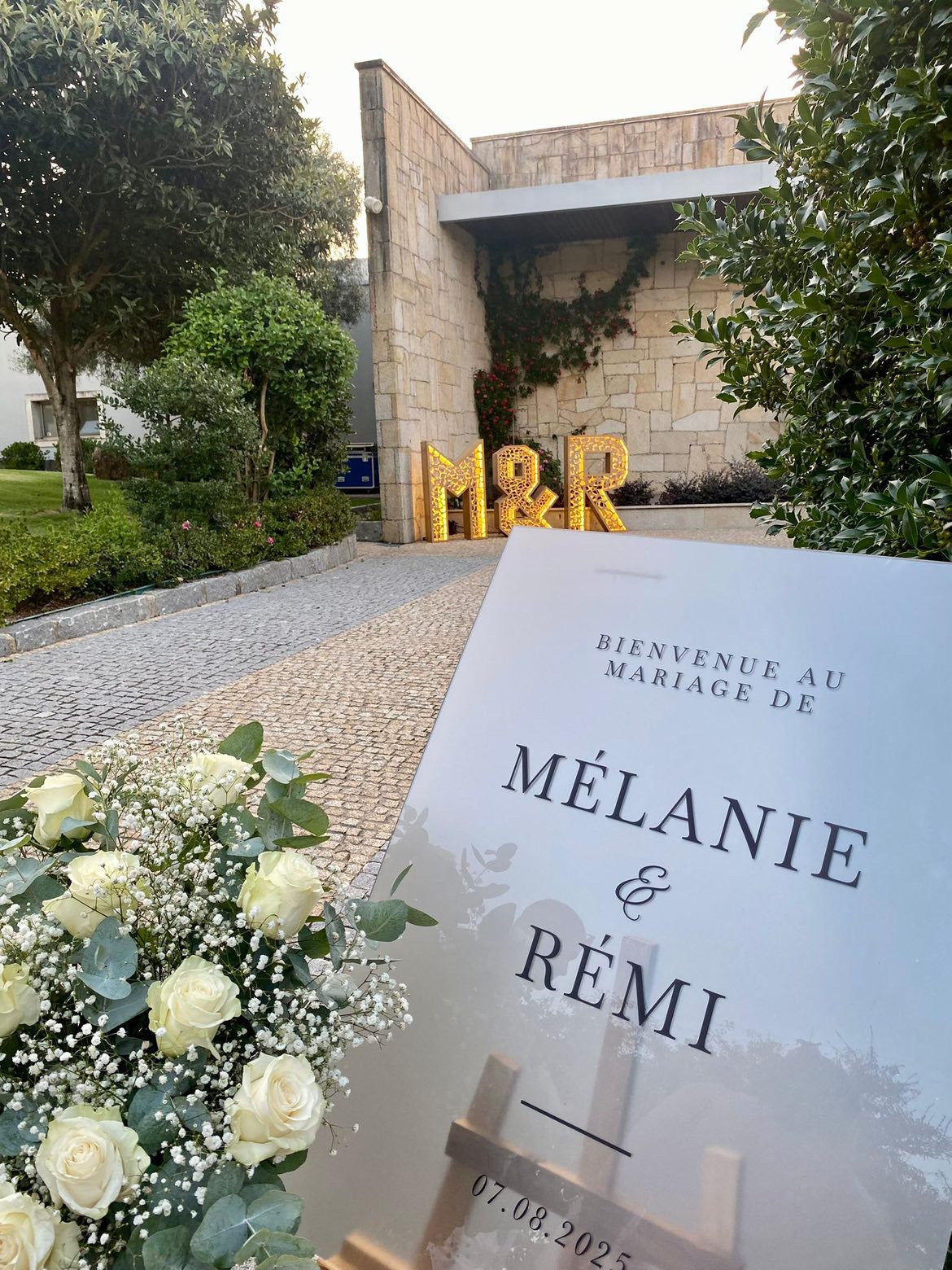 Panneau de bienvenue en plexiglass givré posé sur un chevalet, décoré pour une entrée de mariage élégante.